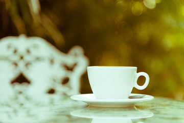A white cup of coffee and silver spoon ready to served in the morning with relaxing and yellow lighting bokeh background.