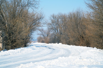 Fototapeta premium Winter snow-covered road with trees at the edges