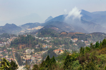 Sa Pa landscape with city, mountains, fog and trees the view from above from Sam Bay Cloud Yard in summer at Ham Rong Mountain Park in Sa Pa, Vietnam.