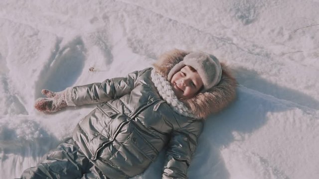 A little girl makes snow angels in snow. Top view.