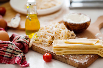 Fresh dough for pasta and pasta machine on kitchen table with ingredients