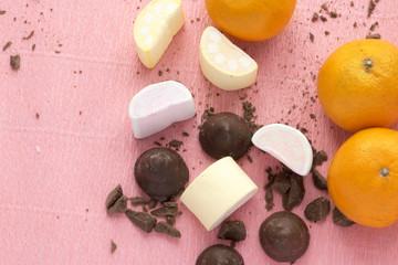 Chocolate candies with orange and marshmallows. Sweets, citrus, desserts on pink background with copy space.