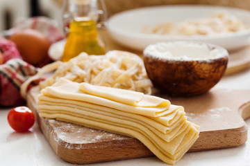 Fresh dough for pasta and pasta machine on kitchen table with ingredients