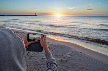 Young girl taking photo - beautiful summer sunset over Baltic sea.