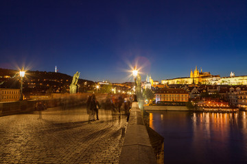 Scenic night view over the Charles bridge with people and castle at the background. Prague, Czech Republic. Illuminated beauty.