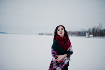 Fototapeta na wymiar Brunette girl in green sweater and red scarf with plaid outdoor frozen lake on evening winter day.
