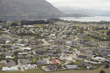 Vista cenital de ciudad a la orilla de un lago y a la falda de una montaña en un día nublado. Wanaka.