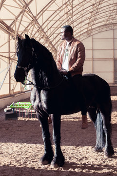 African American Man Riding Black Horse In Hangar