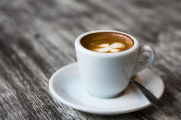 White cup of coffee on plate and spoon with clover leaf shape on top. Break, meeting, leisure time concept