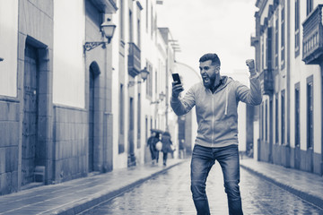 Young man celebrating victory with euphoria in the middle of road on rainy street. Crazy hipster...