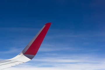 Red and white airplane wing flying on sunny day over blue sky. Plane travel, dream destination, new place concept