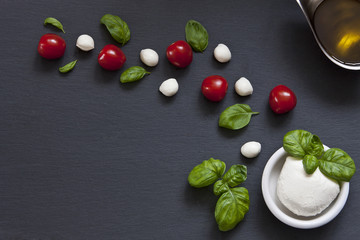 Mozzarella, olive oil, cherry tomatoes and basil on a black stone background. Top view, close-up, background, place for text.