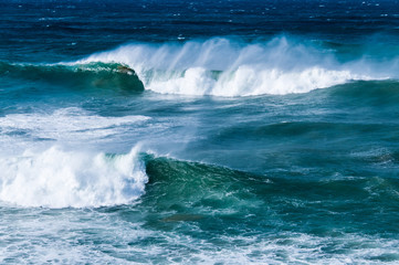 Big waves and strong wind blowing the crest backwards on intense blue sea