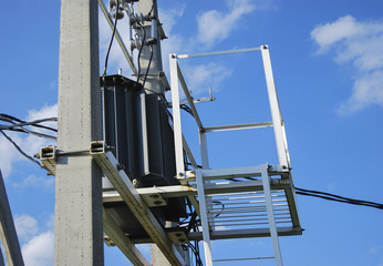An electrical distribution transformer with cooling fins is located on the pole. Against the blue...