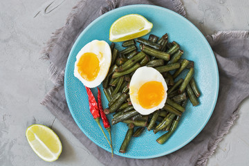 Young green beans stewed with soft-boiled egg on a gray concrete background. Top view, close-up.