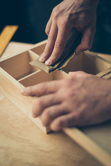 Close up cropped photo of carpenter's hands making smooth the surface on wooden casket using sandpaper he wants to sell his diy