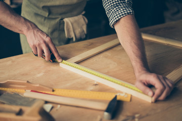 Cropped close up photo of cabinet-maker's strong hands, the master is measuring a wooden frame...