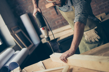 Cropped close up photo of hardworking concentrated confident cabinet maker's hands drilling a hole in wooden plank