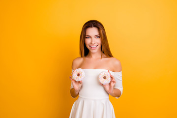 Pretty, charming woman with naked shoulders, holding two white donuts on tits place, wants her boobs to be bigger, standing over yellow background