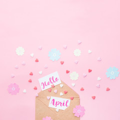 Multicolor sweets sugar candy hearts, handcraft paper flowers and cards with Hello April lettering fly out of craft paper envelope on pink background . Spring concept. Space for text. Square format.