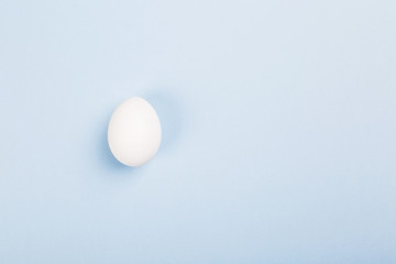 Fototapeta na wymiar White egg on blue background. Top view, copy space