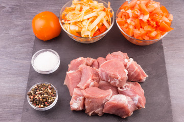 Raw pieces of pork and diced vegetables to extinguish on a dark background