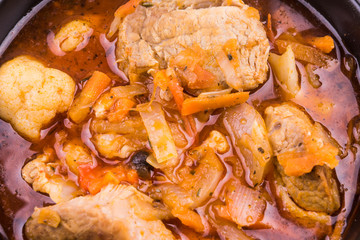 Braised meat with vegetables in a black bowl close-up