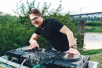 The young DJ-hipster is located behind the mixing console and holds headphones