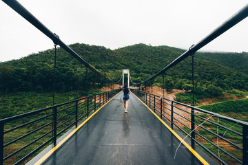 A lady on the bridge travel. Have a mountain and cold day.