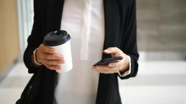 Hands Of Business Woman With Coffee To Go Using Smart Phone