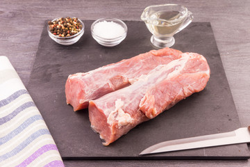 Raw pork tenderloin on a dark background with ingredients for cooking