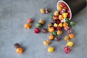 Multicolored popcorn and black paper cup on gray background.