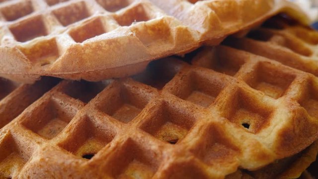 Closeup of fluffy golden brown Belgian waffles in 4k. The pastry baked goods cool on a rack in a kitchen filled with natural light. The breakfast food is a family favorite for delicious Sunday brunch.
