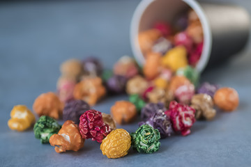 Multicolored popcorn and black paper cup on gray background.