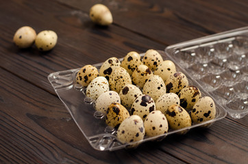 Quail eggs in a plastic container on a dark wooden background. Close up