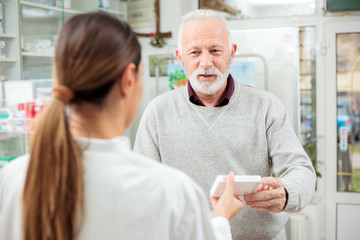 medicine, pharmaceutics, health care and people concept - happy senior man customer buying medications at drugstore