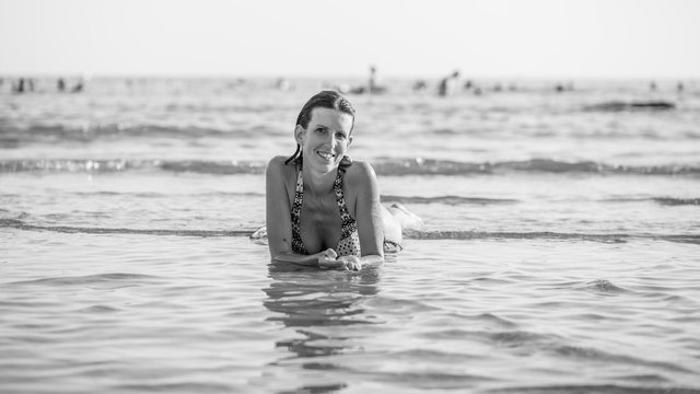 Greyscale image of a smiling woman with wet hair lying in sea