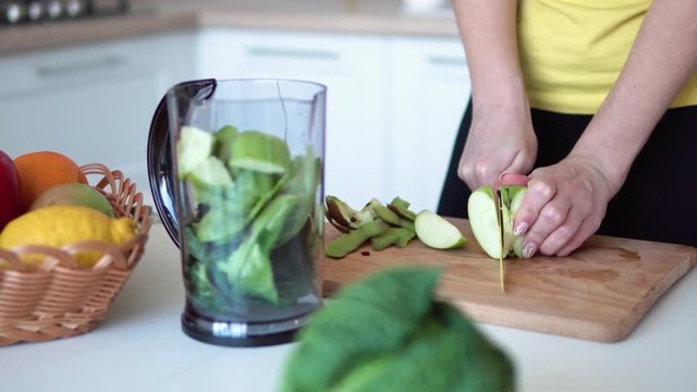 Woman cutting green apple on the chopping board, indoor shot in the kitchen among tasty fruit and vegetables