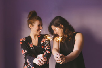 two young beautiful women having fun with sparkles indoors. Purple background. Casual clothing. Fun, happiness and lifestyle