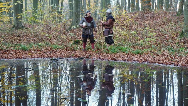 Medieval Vikings talking in the forest near lake and they reflected in water.