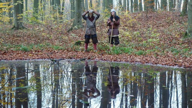 Medieval Vikings talking in the forest near lake and they reflected in water.