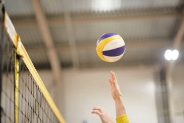 The volleyball player's hand in the covered gym fights the ball in front of the net,