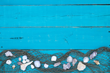 Blank rustic antique teal blue wood sign with seashells and fish netting border; wooden background with copy space