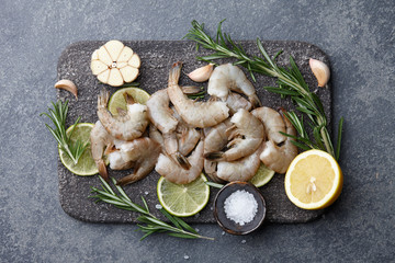 Cooking fresh raw tiger prawns with rosemary, lemon, lime, garlic and spices on stone countertop, top view