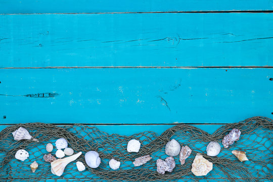Blank rustic antique teal blue wood sign with seashells and fish netting border; wooden background with copy space