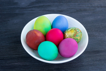 Fototapeta na wymiar White plate with Easter multicolored eggs on black wood