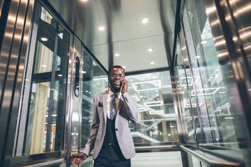Portrait of afroamerican businessman in modern glass elevator talking on phone