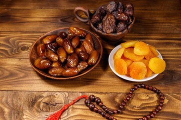 Dried apricots and dates fruit with wooden rosary on wooden table
