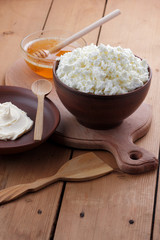 Cheese, fresh cheese and sour cream in pottery, honey, goat cheese for breakfast, healthy eating, healthy dairy products, cheese and cream in rustic style, minimalist, copy space, wooden board