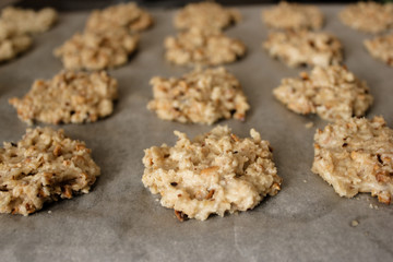 Close up rows of tasty homemade cookies dough before baking. Ready to bake rows of brown oatcakes on baking sheet. Peanut biscuits on baking paper, healthy sweet home-baked products